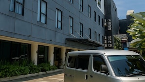 A modern building with a grey facade, multiple windows, and a parked van in front. - Hotel Youstay Semarang By Sinergi (Semarang)