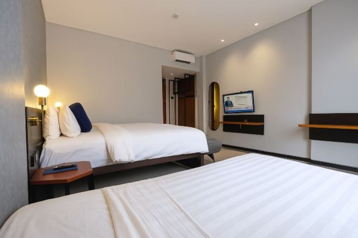 A hotel room with two beds, a desk, a chair, a TV, and a framed certificate on the wall.