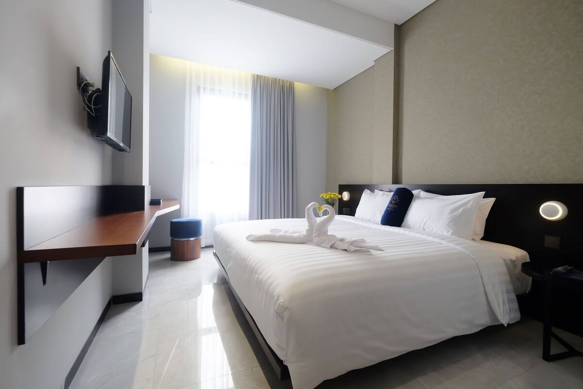 A modern hotel room with a large bed, a desk, and a TV mounted on the wall.