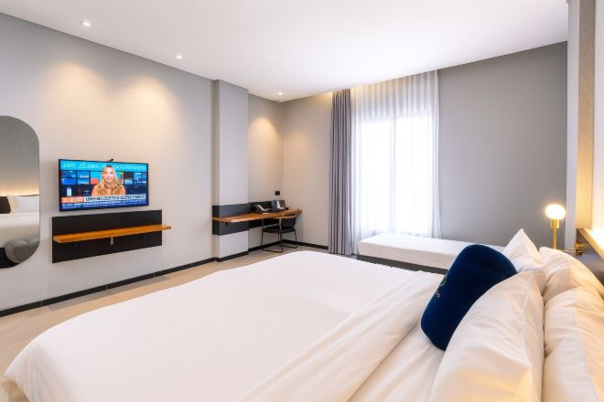 A modern hotel room with a large bed, a desk, a flat-screen TV, and a window with curtains.