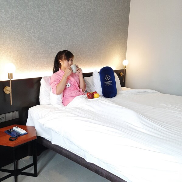 Habitación de hotel con una cama, una mesita de noche con un teléfono y un libro, y una pared con una lámpara.