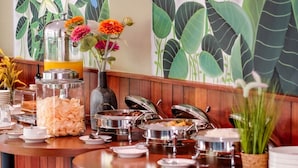 A buffet setup with various food containers and a decorative vase with flowers. - Hotel Youstay Semarang By Sinergi (Semarang)