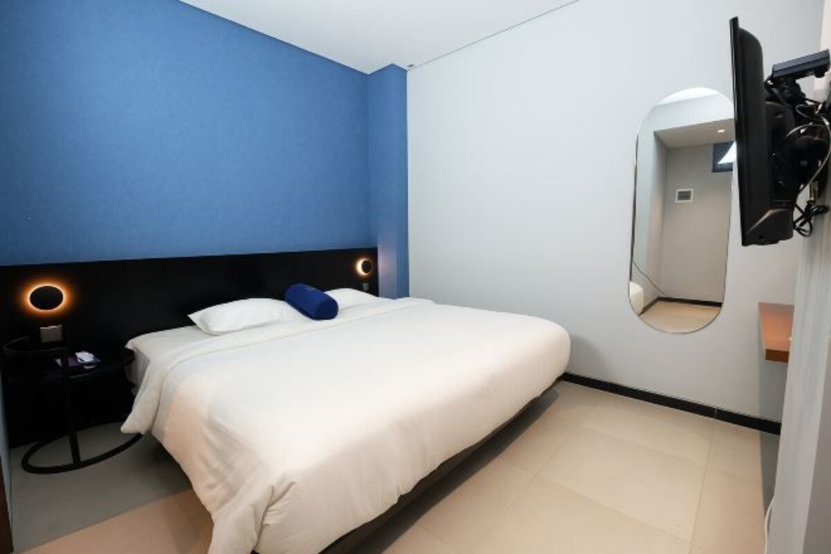 A modern hotel room with a bed, a round mirror, and a nightstand with a lamp.