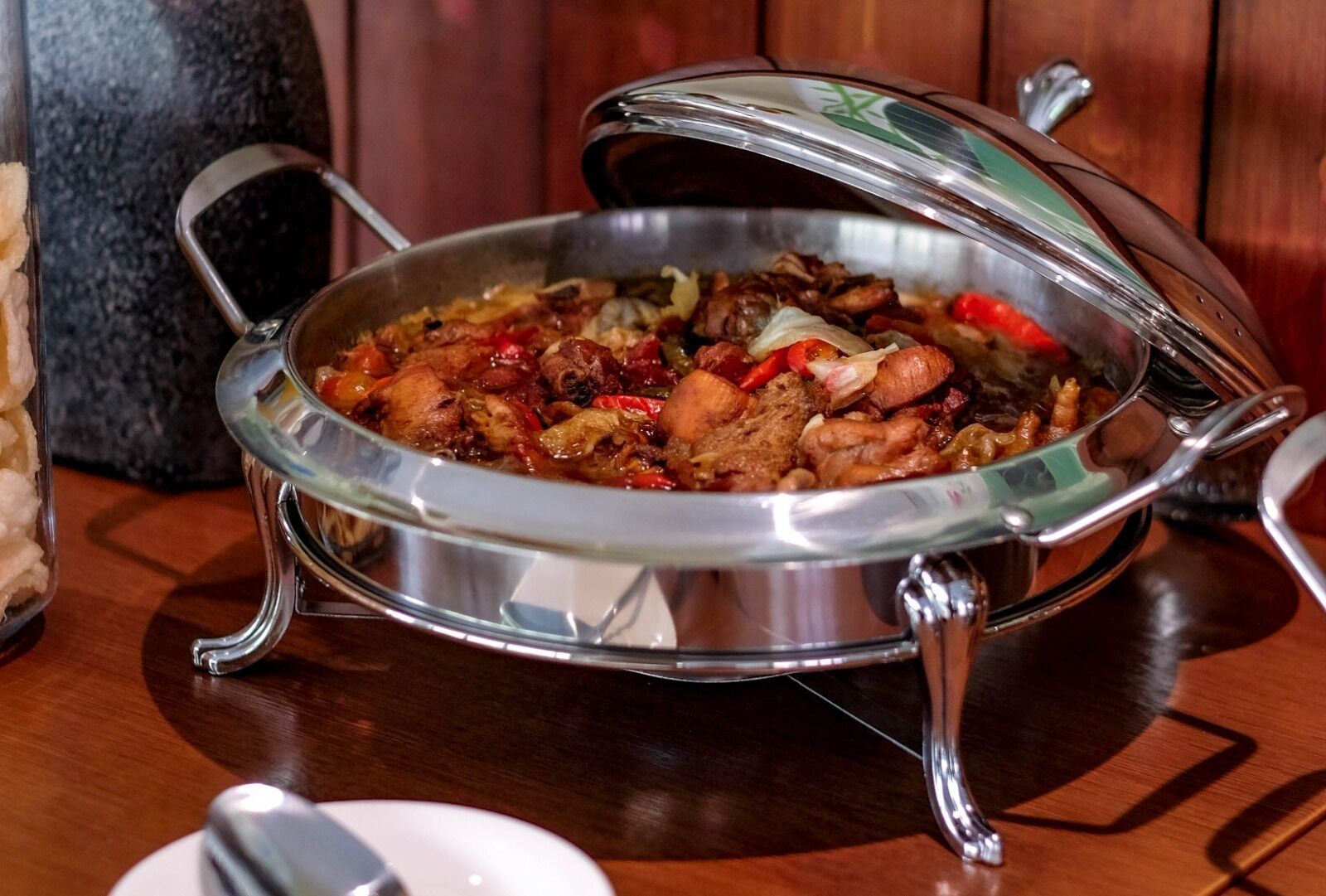 Un recipiente metálico con tapa, que contiene un plato con carne y verduras, sobre una mesa de madera.