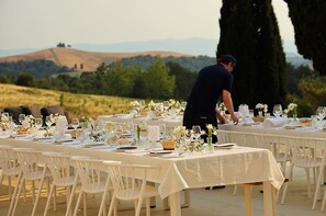 An outdoor dining setup with white tablecloths and chairs, a waiter in the background, and a scenic view of hills and trees. - Villa Casa Collina - Castelfalfi - Tuscany - Saltwater pool- Airco & VIP Service (Castelfalfi)