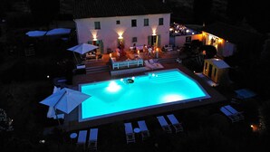 Una amplia piscina al aire libre con sillas de descanso y sombrillas, rodeada por un edificio con múltiples ventanas y zonas de estar exteriores.