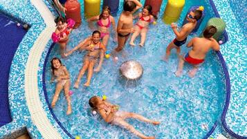 Niños jugando en una piscina mientras adultos vigilan.