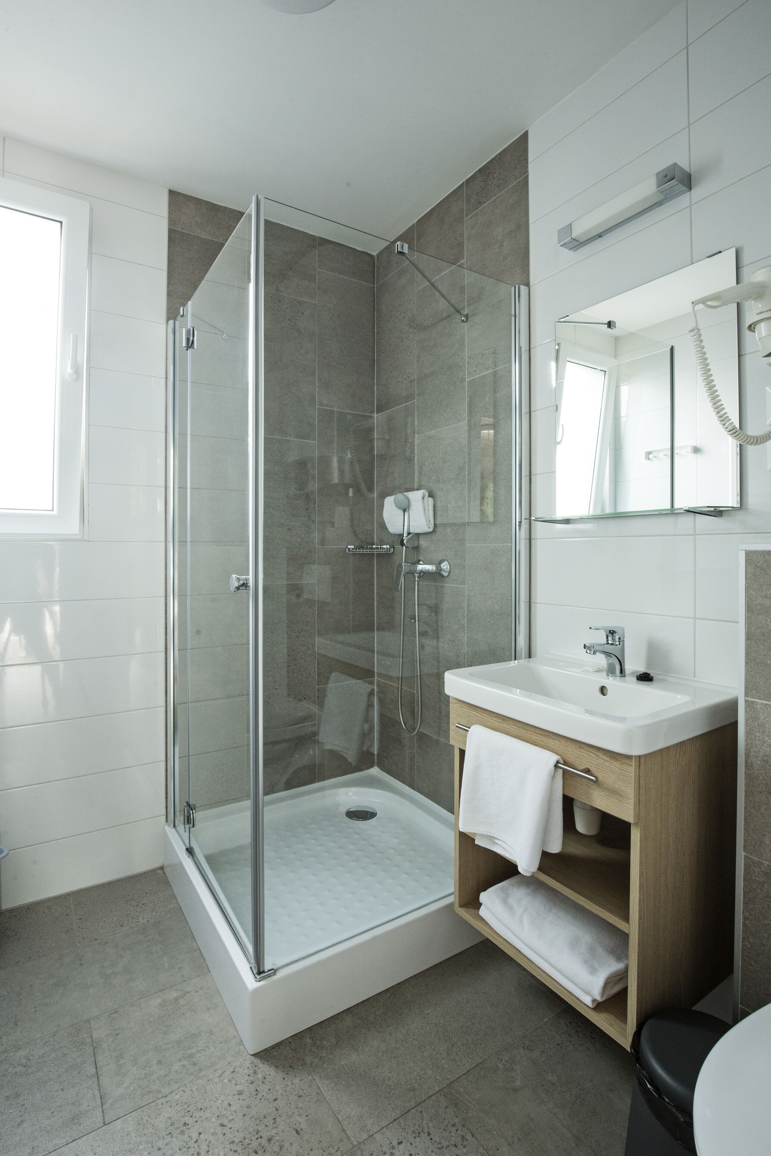 A modern bathroom with a glass-enclosed shower, a white sink, and a wooden vanity.