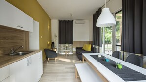 A modern kitchen with a wooden countertop and white cabinets, a dining area with a white table and benches, and a sofa with yellow cushions. - Barack Thermal Apartments (Tiszakécske)