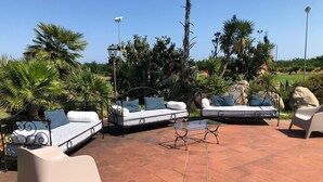 An outdoor patio area with three white sofas and a glass coffee table. - Casa Felice Due - Contrada Guido (con piscina) (sellia marina)