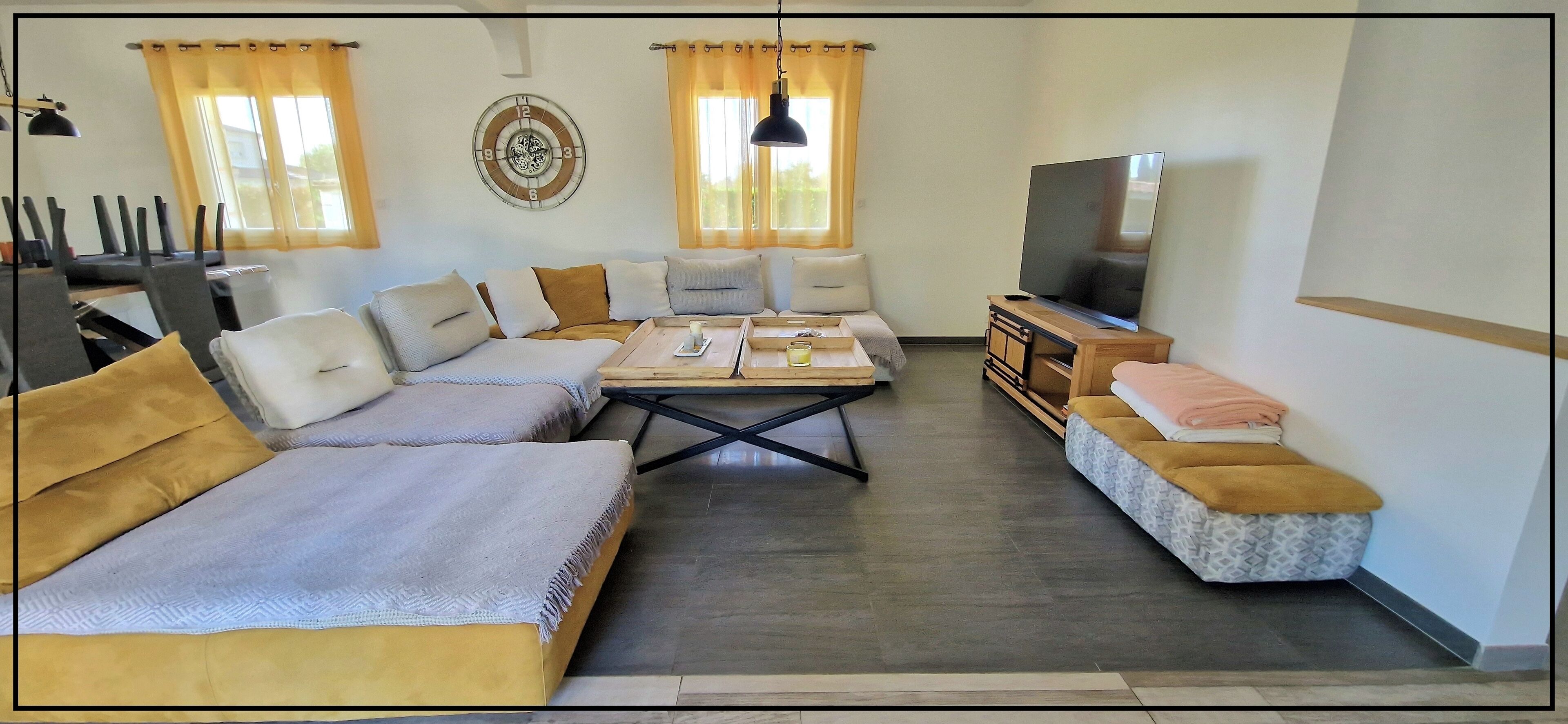 A living room with a sofa, armchairs, a coffee table, a TV, and a dining area with chairs and a table.