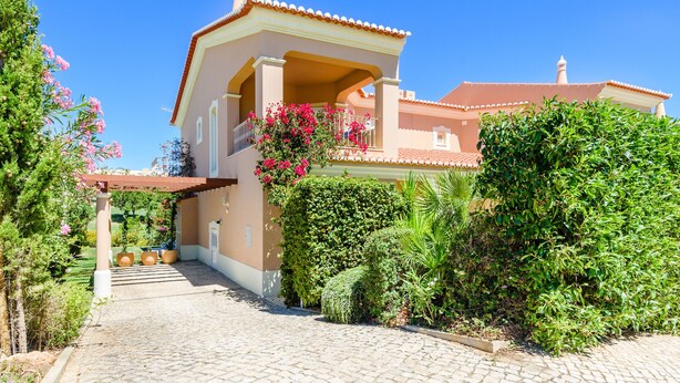 A house with a covered porch, a garden with various plants and flowers, and a clear blue sky.