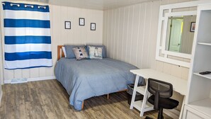 Une chambre à coucher avec un lit, un bureau, une chaise, une fenêtre et un rideau à rayures.