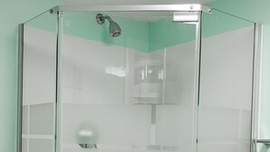 Une cabine de douche fermée par des parois en verre, équipée d’un pommeau de douche, d’un sèche-mains et d’une petite étagère.
