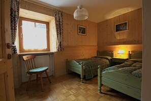 A room with wooden walls, a window with curtains, a chair, two beds, and a hanging light fixture. - Comfortable Ground Floor Apartment in Sesto (Sesto)