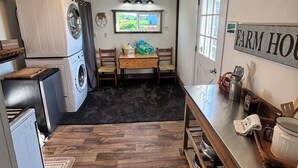 Una cucina compatta con zona pranzo, lavatrice, frigorifero e un cartello con la scritta 'FARM HOUSE'.