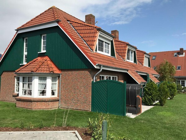 Una casa de dos pisos con fachada verde, tejas rojas y una chimenea de ladrillo.