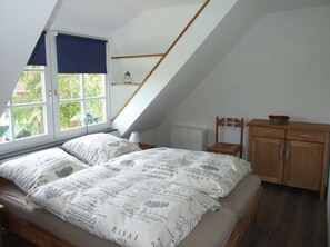 Un dormitorio con techo inclinado, una cama con ropa de cama estampada, un armario de madera y una ventana con vistas a la vegetación.