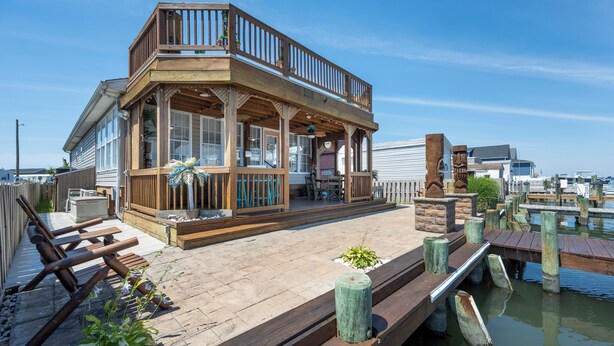 A wooden deck with a covered seating area, a view of the water, and a dock extending into the water. - Outdoor Living At it's Finest With this Vacation Home! (Ocean City)