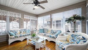 A sunroom with wicker furniture, large windows, and a ceiling fan. - Outdoor Living At it's Finest With this Vacation Home! (Ocean City)