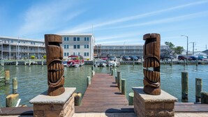 A wooden pier leading to a marina with boats, a building with balconies, and a clear sky. - Outdoor Living At it's Finest With this Vacation Home! (Ocean City)