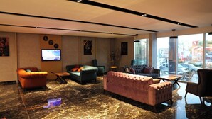 A modern lobby with a marble floor, multiple seating areas including sofas and armchairs, a flat-screen TV mounted on the wall, and large windows offering a view of the city. - Grand Merpond Otel (Merzifon)