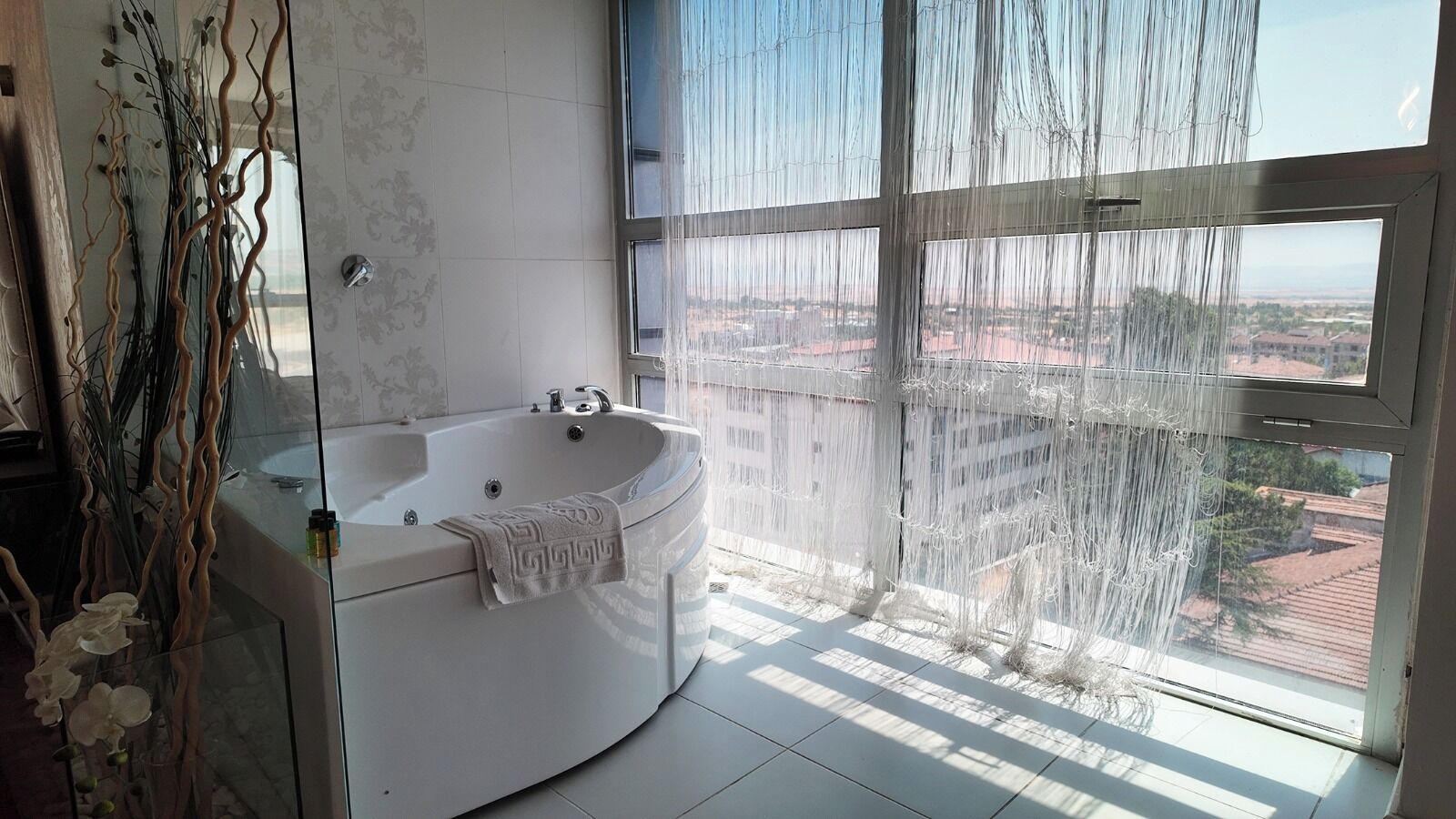 A modern bathroom with a freestanding bathtub, a glass shower enclosure, and a view of a cityscape through large windows.