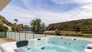 A hot tub with a glass enclosure, overlooking a coastal landscape with hills and palm trees. - ❤ BEACHFRONT & JACUZZI ❤ Casa 4Brothers (Cala en Porter)