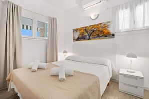Hotellihuone, jossa on sänky, yöpöytä, taulu ja ikkuna, jossa on verhot.