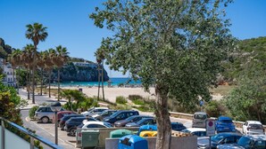 A parking lot with cars, a tree, and a beach in the background. - ❤ BEACHFRONT & JACUZZI ❤ Casa 4Brothers (Cala en Porter)