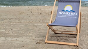 A beach chair with a logo and text on it, placed on a sandy beach with the ocean in the background.