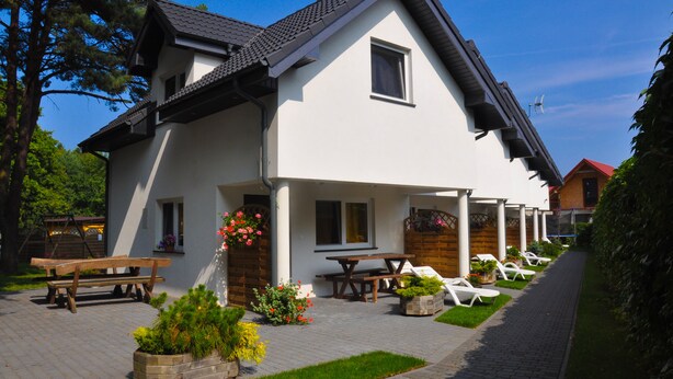 A two-story house with a patio area featuring a wooden bench, a picnic table, and several lounge chairs.