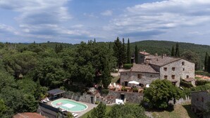 Edifici de pedra amb piscina i zona d'estar a l'aire lliure, envoltat d'arbres.