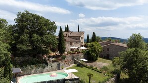 Edifici de pedra amb una piscina, envoltat d'arbres i un cel clar.