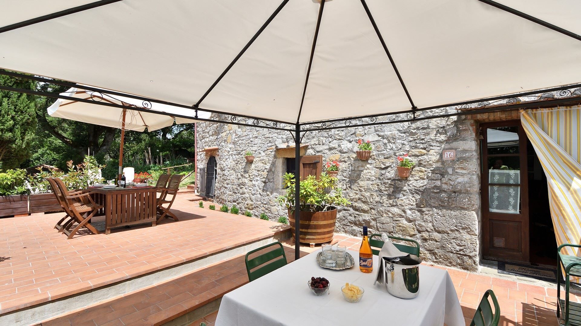 Un patio exterior con una mesa lista para comer, rodeado de muros de piedra y plantas en macetas.