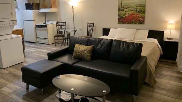 A compact hotel room with a bed, a black leather sofa, a small table, a dining area with chairs, a kitchen with a microwave, and a painting on the wall. - 1326-#9 Comfy studio in downtown  (San Antonio)