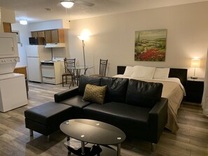 A compact hotel room with a bed, a black leather sofa, a small table, a dining area with chairs, a kitchen with a microwave, and a painting on the wall. - 1326-#9 Comfy studio in downtown  (San Antonio)