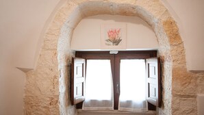 Un arco de piedra con dos contraventanas de madera abiertas y una obra de arte floral enmarcada arriba.