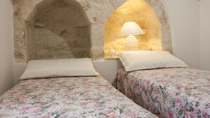 Un dormitorio con dos camas, cada una con ropa de cama floral, una pared de piedra y una ventana con una lámpara.