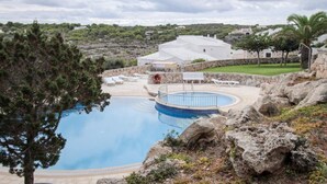 A pool area with a circular hot tub, lounge chairs, and a stone wall. - Villas es Brucs - 5 - 2 (Cala Morell)