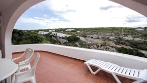 A balcony with white chairs and a table, overlooking a rocky landscape with white buildings. - Villas es Brucs - 5 - 2 (Cala Morell)