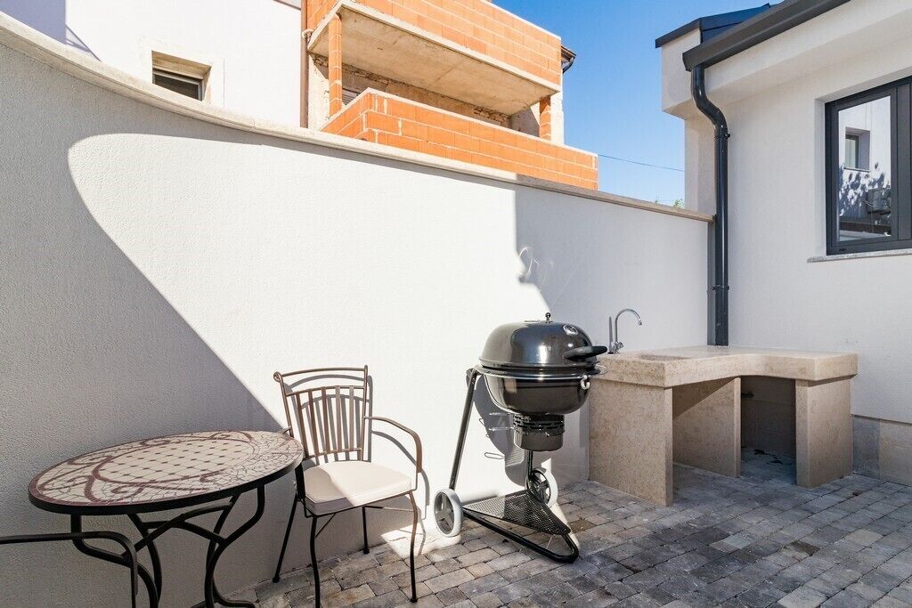 A patio with a round table and a chair, a barbecue grill, and a concrete sink.
