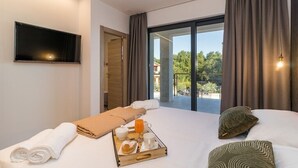 A modern hotel room with a large bed, a breakfast tray, a flat-screen TV, and a balcony with a view of greenery.