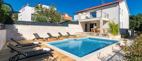A modern villa with a swimming pool, sun loungers, and a wooden deck.