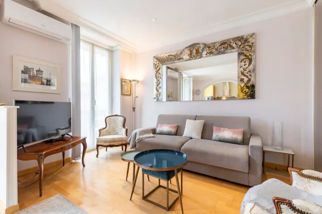 Un salon moderne avec un canapé gris, une table basse ronde, un téléviseur et un grand miroir décoratif.
