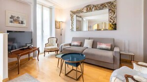 A modern living room with a grey sofa, a round coffee table, a television, and a large decorative mirror. - Charming flat Carré d'Or/Musiciens, 5 min away from the beach, WIFI (Nice)