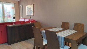 Ein modernes Wohnzimmer mit Essbereich, einem roten Sofa, Holzstühlen und einer Chandeliebre.