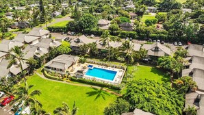 An aerial view of a resort with multiple bungalow-style buildings, a central swimming pool, and a backdrop of a beach and ocean.