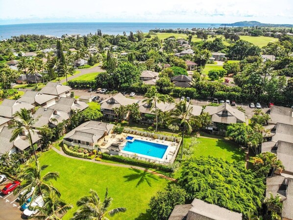 Vista aérea de un resort con varias construcciones tipo bungalow, una piscina central y un fondo de playa y océano.