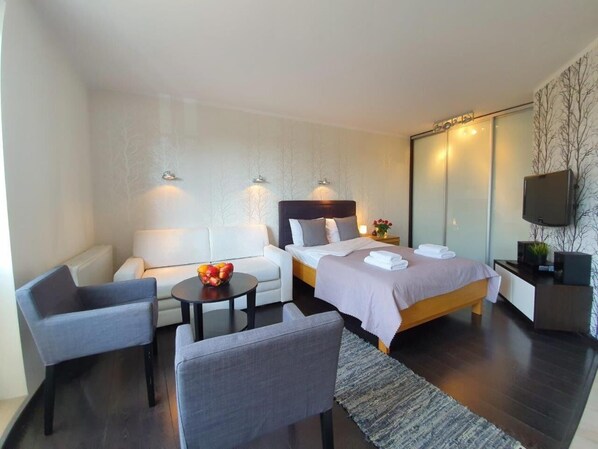 Quarto de hotel moderno com cama, sofá, mesa pequena e televisão.